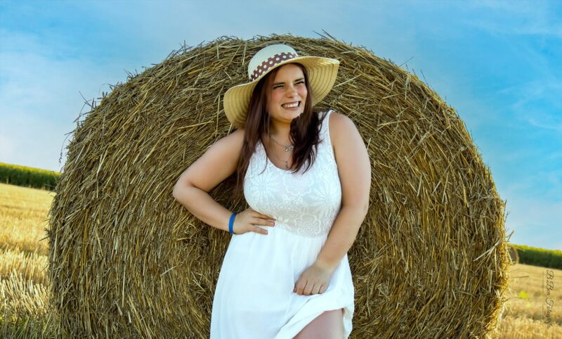 Egyéni női portréfotó, naplementében a szalmabálák közt.